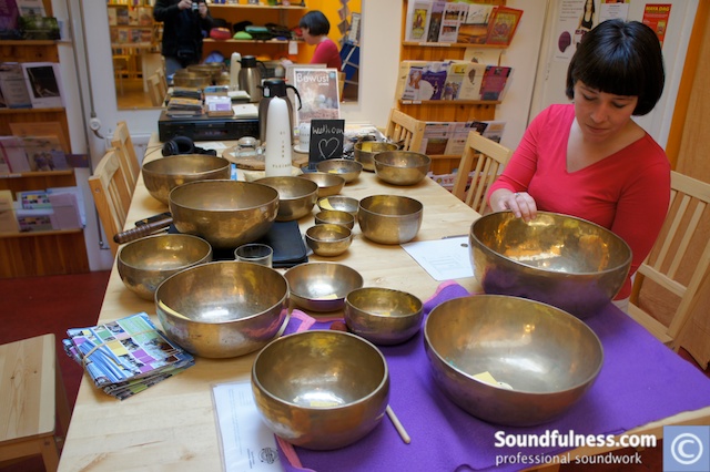 Practitioner selecting from a table of singing bowls in a shop setting