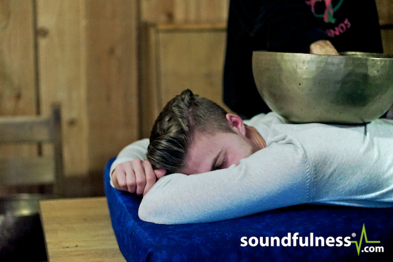 Client lying face down as Coen places a singing bowl on the back of the head