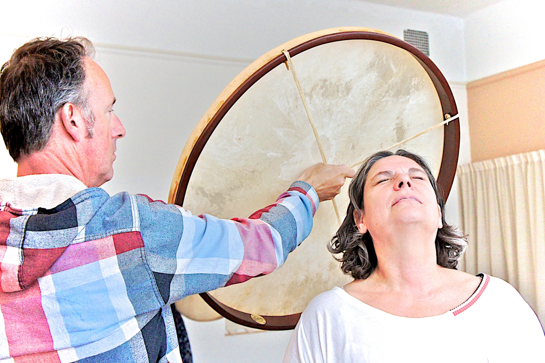 Coen playing a large frame drum next to a seated participant's head
