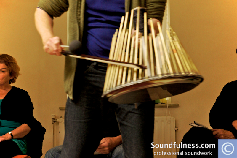 Practitioner playing a waterphone in front of a seated circle