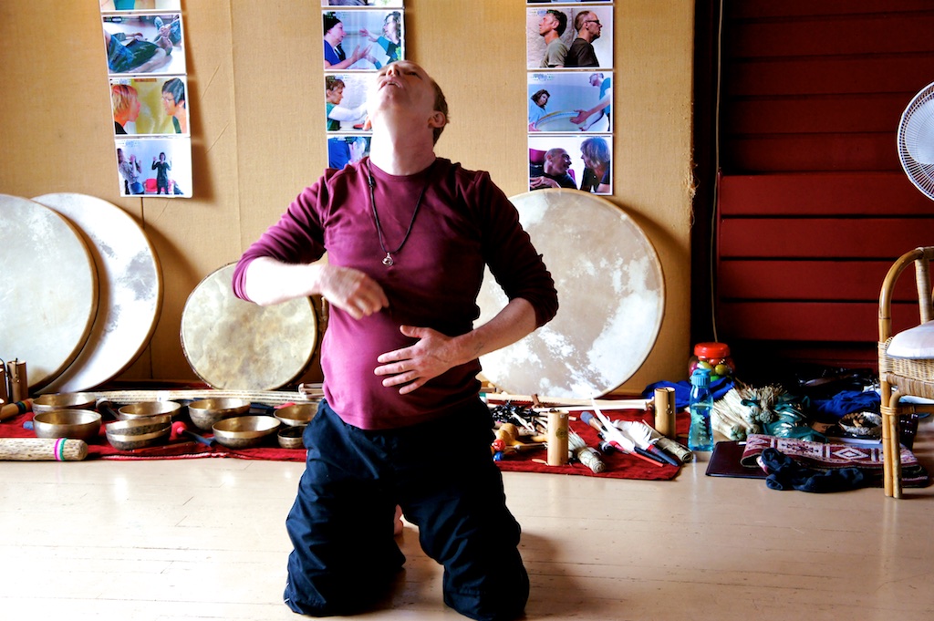 Coen kneeling in an embodied movement in front of frame drums and singing bowls