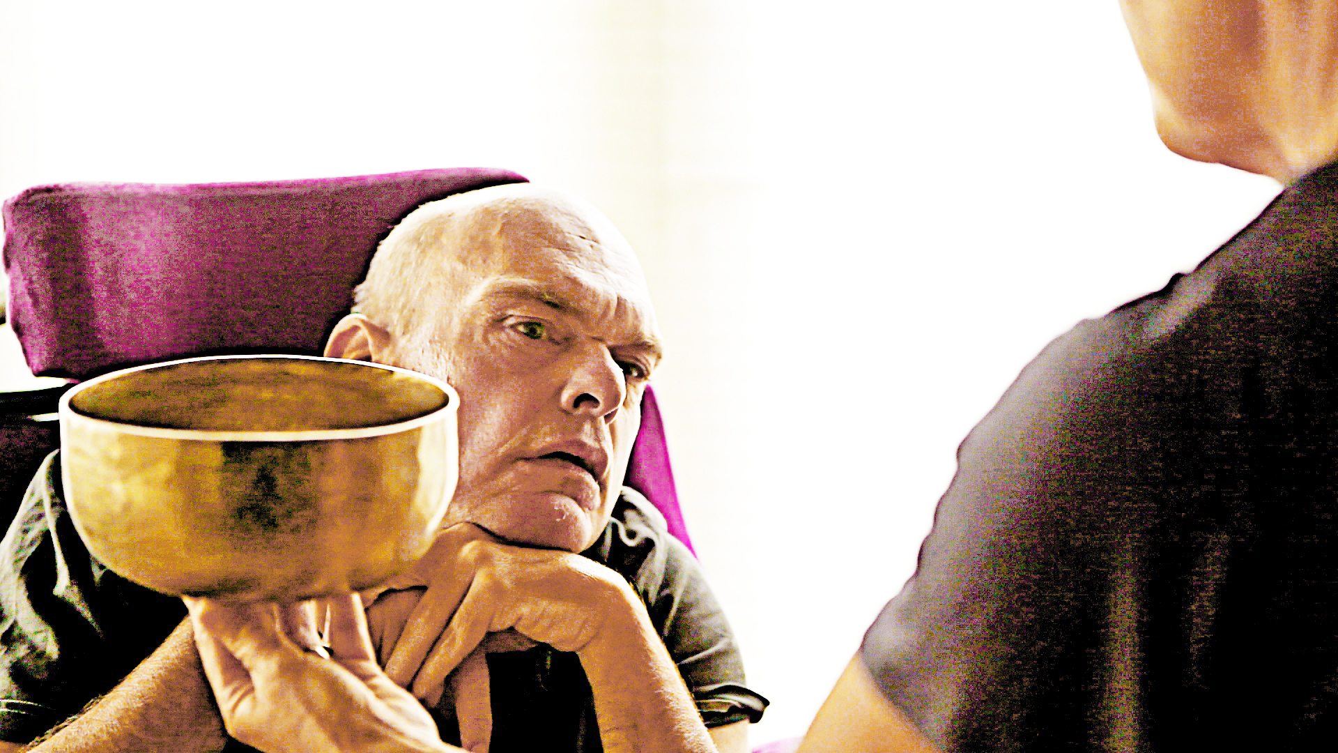 Older man in a purple recliner resting his chin on a singing bowl held in his hands