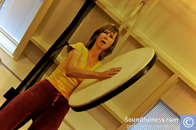 Woman in yellow top playing a large frame drum in a bright practice room
