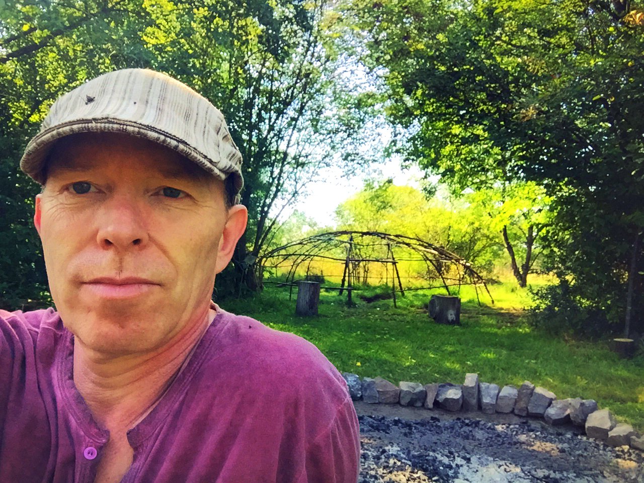 Coen in front of a sweat lodge frame in a forest clearing