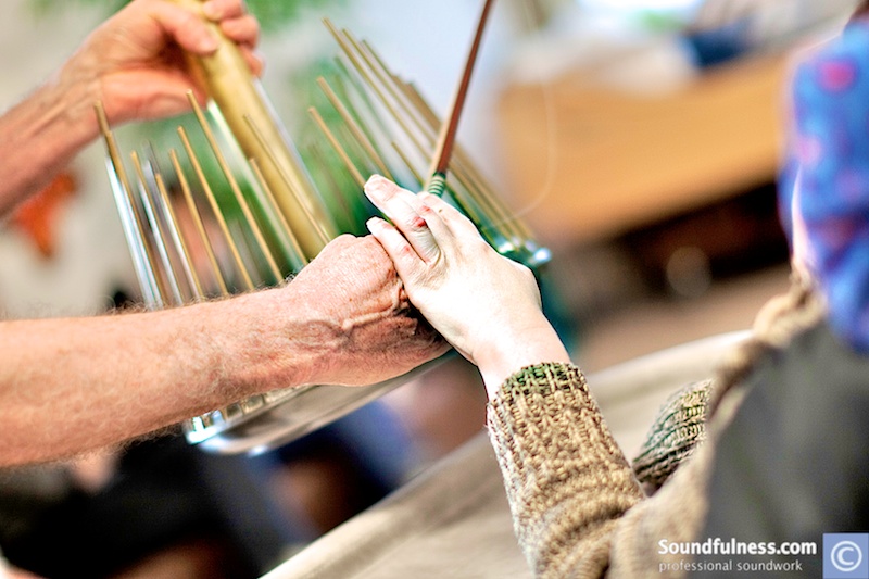 Close-up of hands guiding a client's fingers along the rods of a shanti chime