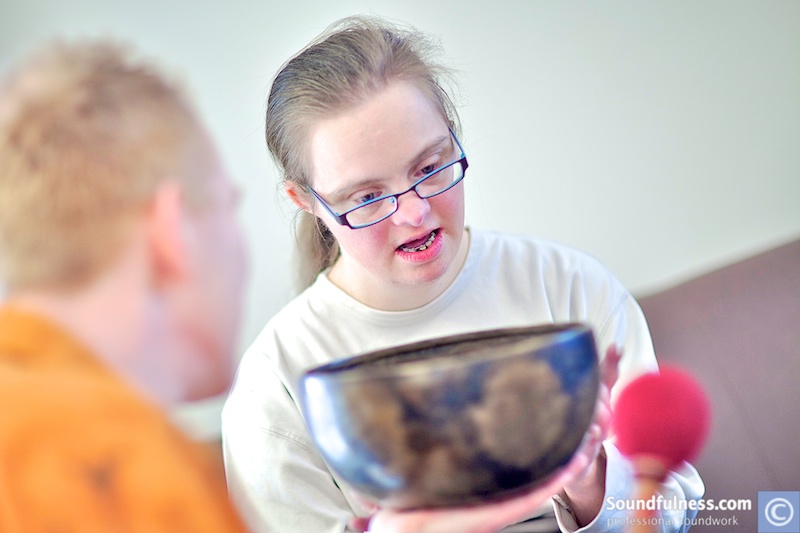 Young woman with Down syndrome holding a singing bowl in dialogue with practitioner