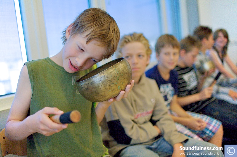 Boy holding a singing bowl close to his ear with a mallet in hand