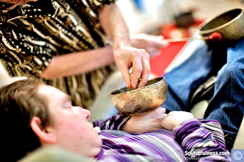 Singing bowl resting on a reclining client's chest while hands play surrounding bowls