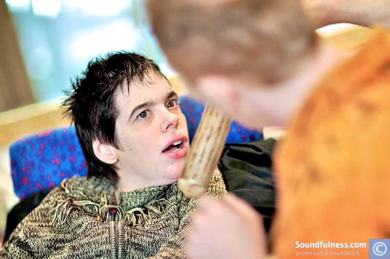 Young man in a care setting looking at a wooden mallet held by the practitioner