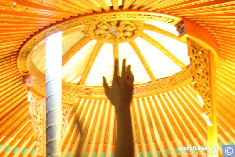 Looking up at the ornate crown of a yurt with a raised hand