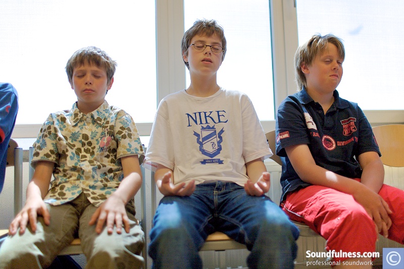 Three young boys seated in a school classroom with eyes closed in a moment of stillness