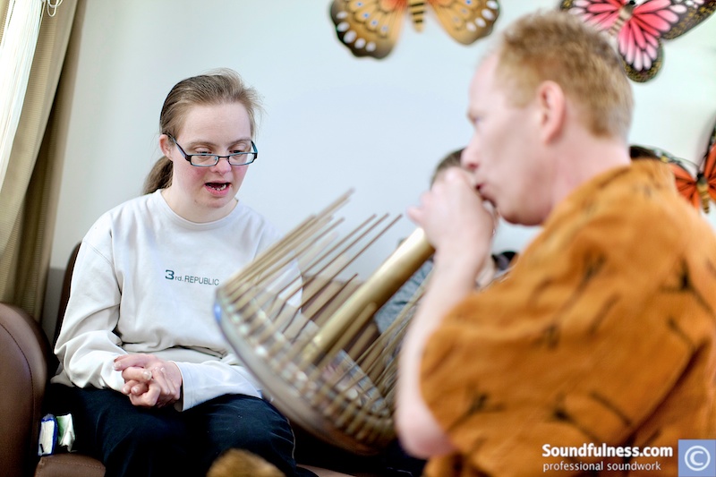Young woman with Down syndrome listening as practitioners play shanti chime and rainstick
