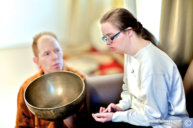 Practitioner offering a large singing bowl to a young woman during a care session