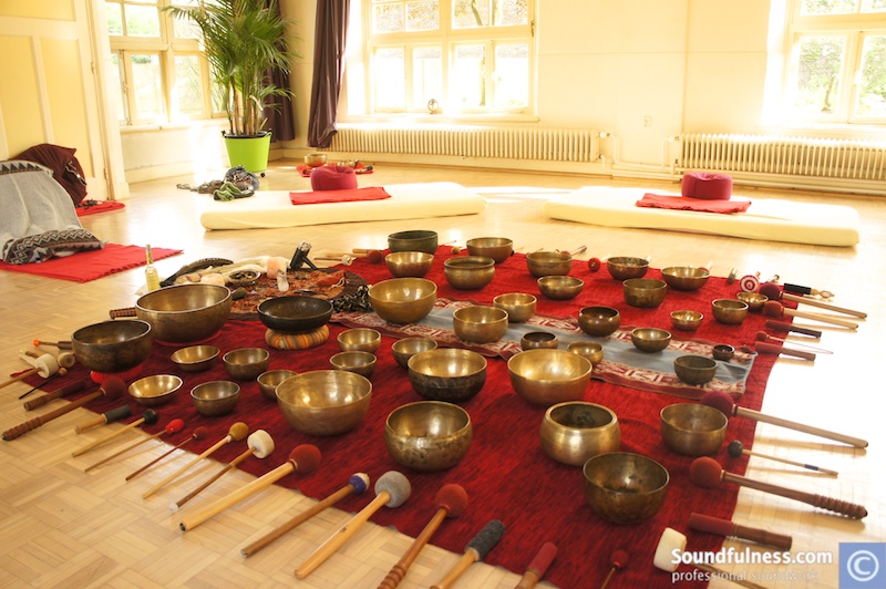 Wide array of singing bowls and mallets laid out on a red rug for a masterclass