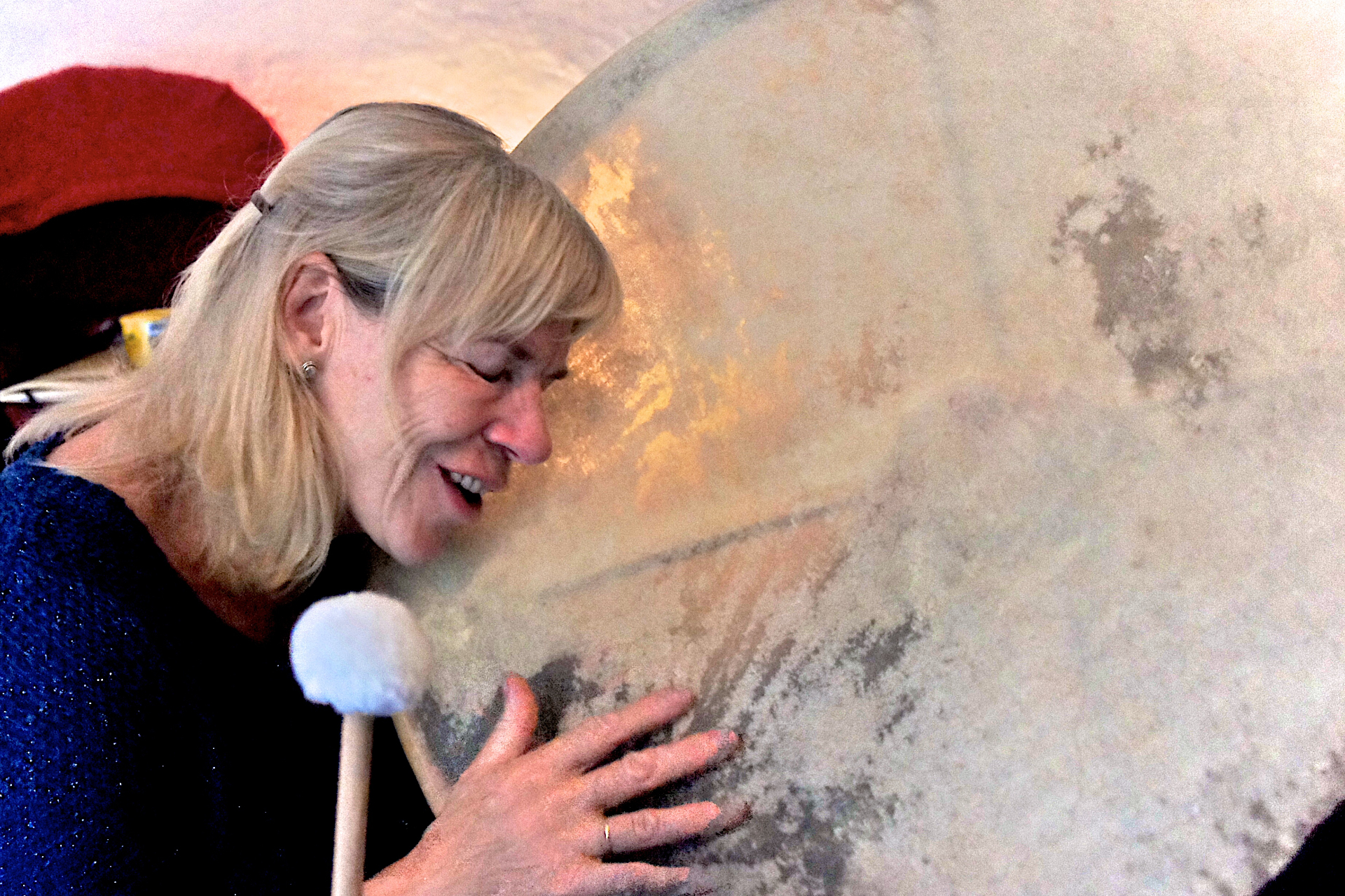 Woman resting her head against a large gong with a soft mallet