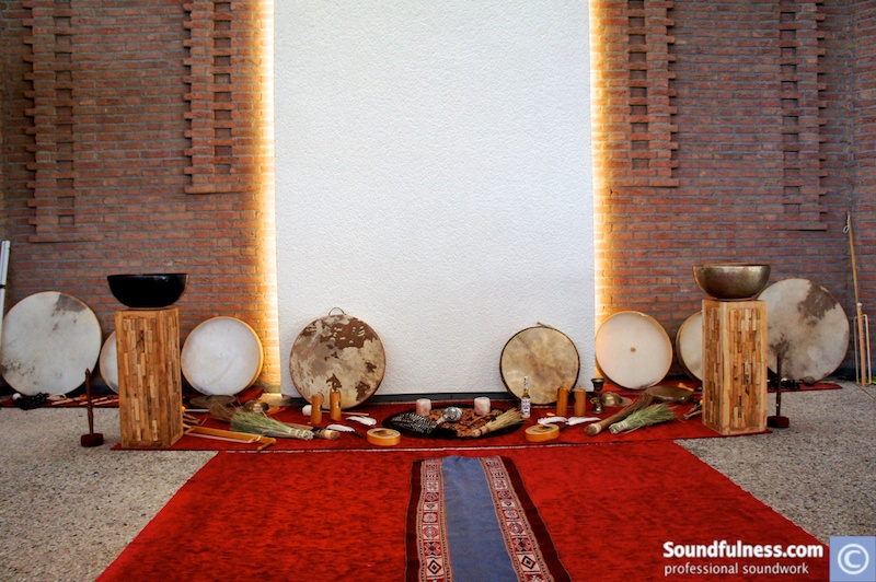Symmetrical wall of frame drums, singing bowls and offerings against a warm brick backdrop