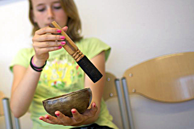 Young girl in green shirt playing a small singing bowl with a wooden mallet