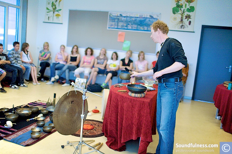 Coen demonstrating singing bowls and a gong to a classroom of seated students