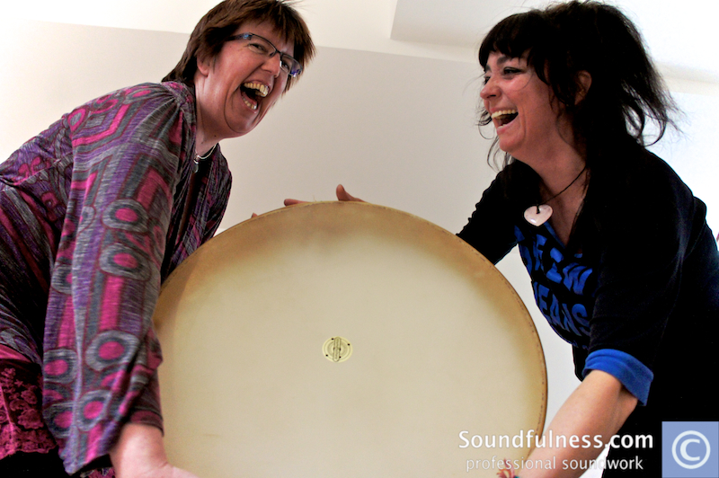 Two women holding a large frame drum between them, laughing