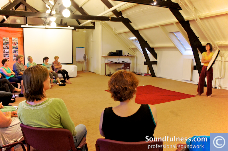 Attic training room with participants seated in a circle and teacher standing on a red carpet