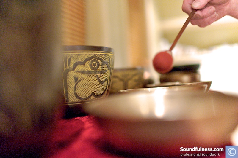 Close-up of a hand striking a Tibetan singing bowl with a red felt mallet
