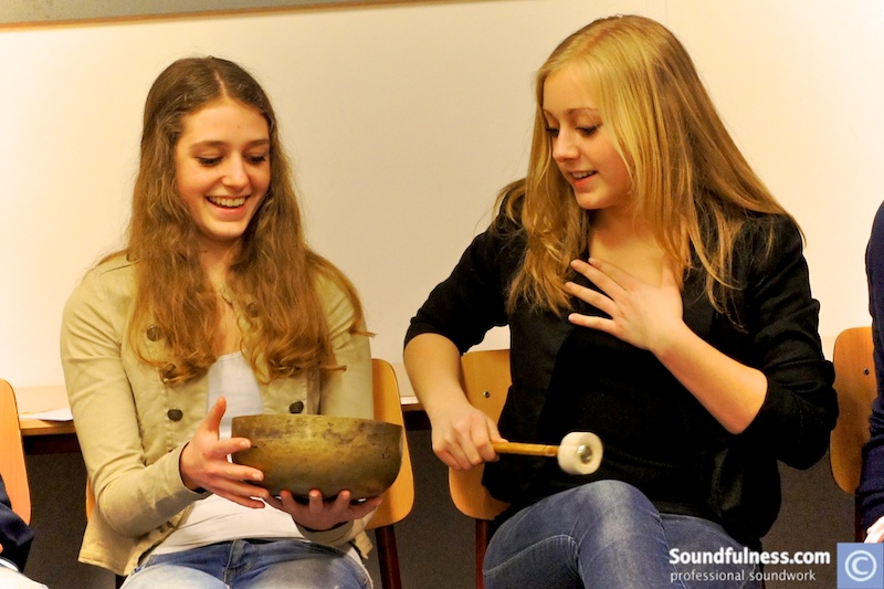 Two teenage girls smiling while playing a singing bowl together